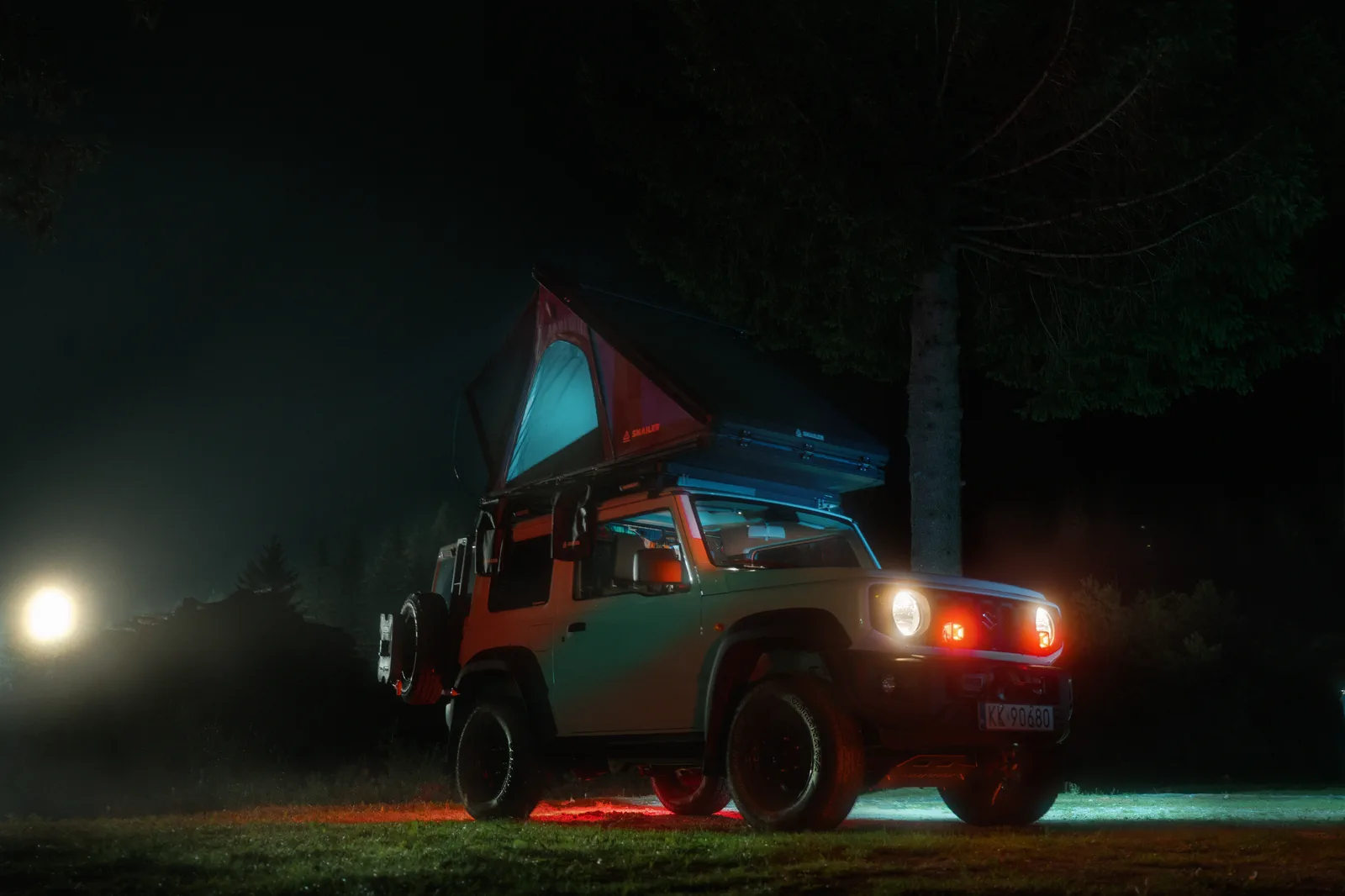 Off-road vehicle with an illuminated SNAILER roof tent at night